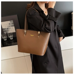 Detail of a large brown PU leather tote bag with gold metal hardware on model's shoulder