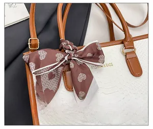 Detail of white snakeskin tote bag with brown leather handles and heart-patterned silk scarf