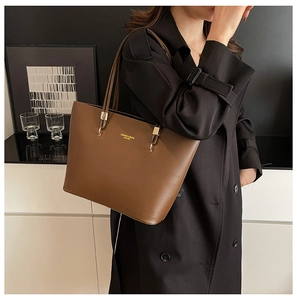 Detail of a brown leather tote bag with gold lettering and slim shoulder straps