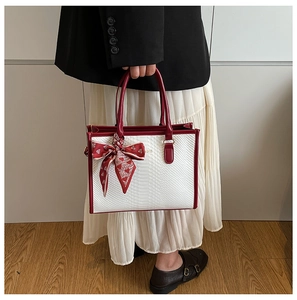 Close-up of white snake pattern tote bag with red leather trim and silk scarf detail