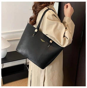 Detailed side view of a large black PU tote bag with gold logo on a female model