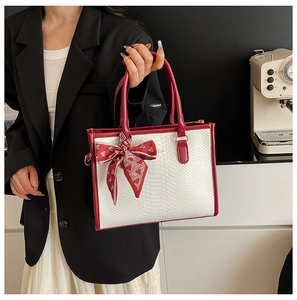 Detail of white snake-textured tote bag with red handles and heart scarf bow charm