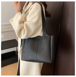 Detailed side view of minimalist black tote bag with slim shoulder straps on a beige coat