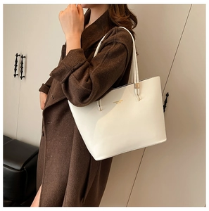 White leather tote bag with gold lettering shown worn on a brown woolen coat