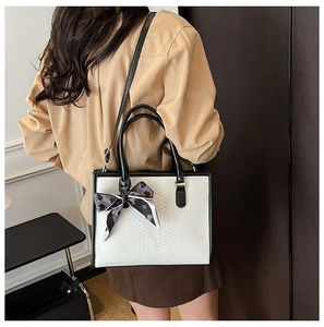 Detail of white snakeskin tote bag with black handles and elegant silk scarf decoration