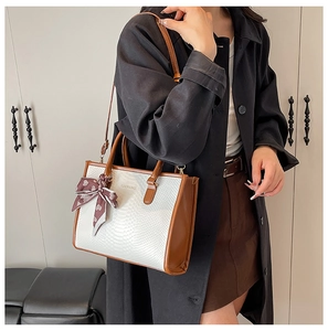 Detail showing white snake pattern texture and brown leather trim on a tote bag
