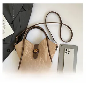 Detailed view of pleated bucket bag with metal lock showing scale against a laptop and phone