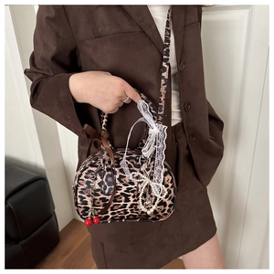 Détail du sac à main léopard avec nœud en soie, dentelle blanche et breloque cerise