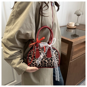 Détail d'un sac bandoulière léopard avec poignées rouges et nœud en dentelle élégant