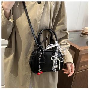Détail du sac à nœud en cuir noir avec pendentif cerise et dentelle sur un trench-coat
