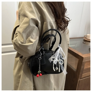 Gros plan d'un sac à main noir avec charm cerise rouge et nœud en dentelle aux perles blanches