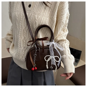 Detail of a brown leather crescent handbag with cherry and pearl bow charms and lace knots