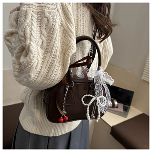 Detail of dark brown leather pillow bag with red cherry charm and pearl bow accessories