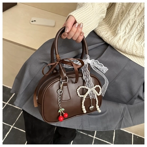 Close-up of brown boston bag with lace ribbons, pearl bow charm and cherry pendants
