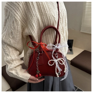Detail of red leather crossbody bag with lace, ribbon bows, and cherry pendant charm