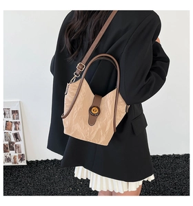 Detail of light khaki textured bucket bag with brown leather strap worn by a model