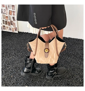 Detalle del bolso tipo cubo plisado beige con asa redonda marrón y hebilla dorada
