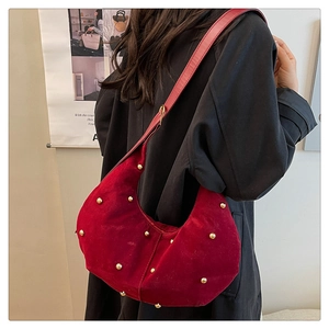 Close-up of red suede crescent bag featuring decorative gold studs and shoulder strap
