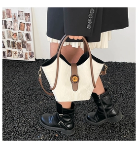Detail of cream bucket bag featuring brown trim and wave edge design with metal clasp