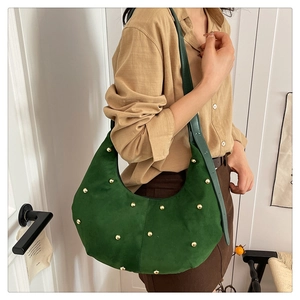 Dettaglio di borsa a mezzaluna in camoscio verde scuro con borchie dorate e tracolla