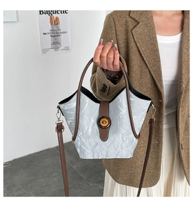 Macro view of light gray crinkled textured bucket bag with brown leather strap detail