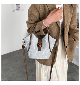 Detail of silver pleated bucket bag with brown leather trim and golden metal lock