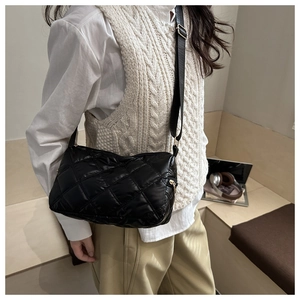 Detail of black quilted puffer crossbody bag with wide strap and gold hardware