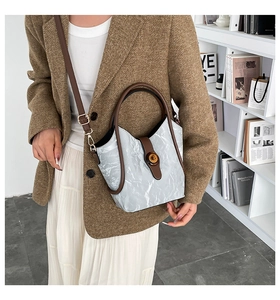 Detailed view of grey textured bucket bag with brown leather handles and metal twist lock