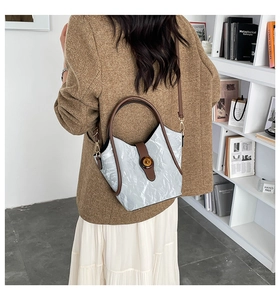 Detalle del bolso de hombro azul grisáceo con textura plisada y correa de cuero marrón