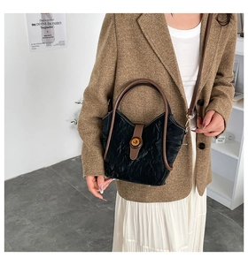 Detail of black pleated bucket bag with brown leather strap and metal buckle lock