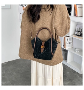 Detail of black pleated textured bucket bag with brown handles and metallic buckle