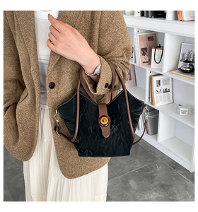 Detail of black pleated texture handbag with brown leather trim and resin buckle lock