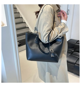 Detail van een zwarte leren shopper met een kleine olifant hanger op een strakke trap