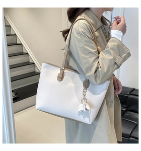 Close-up of a white tote bag featuring beige long handles and an elephant charm detail