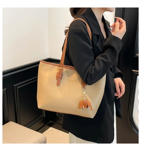 Model wearing large beige tote bag with brown straps and cute elephant charm