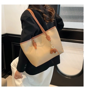 Detail van beige shopper tas met bruine hengsels en olifant hanger gedragen door model