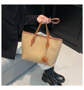 Detail van beige shopper met bruine handvatten en een leren olifantenhanger accessoire