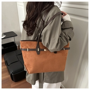 Detailed side view of brown faux suede tote bag with gold lock and strap being worn
