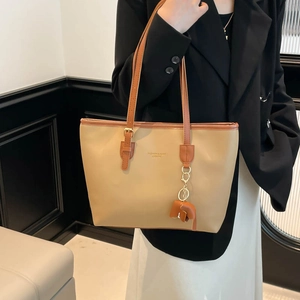Large beige tote bag with brown trim and elephant charm shown on model in studio