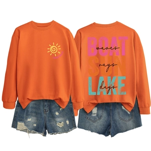 Flat lay of an orange Lake Days sweatshirt with back graphic and denim shorts set
