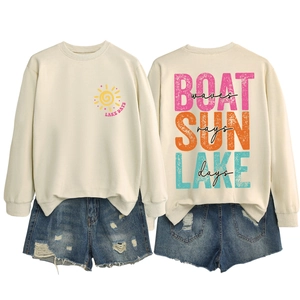Flat lay view of a beige sweatshirt showing Lake Days graphic and distressed denim shorts