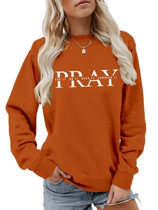 Detail of orange sweatshirt featuring white PRAY letter print paired with blue denim jeans