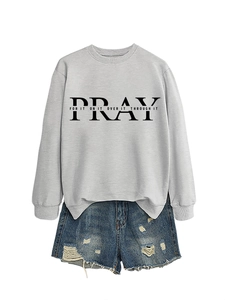 Detail of grey crewneck sweatshirt with PRAY lettering and ripped denim shorts