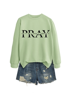 Detailed flat lay of mint green sweatshirt with PRAY slogan and distressed denim shorts