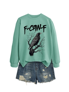 Dettaglio flat lay della felpa verde menta con stampa corvo e pantaloncini di jeans usurati