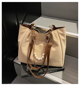 Dettaglio della borsa tote beige con logo in metallo dorato, perle e catene sottili