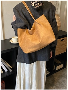 Detail of a large brown suede tote bag showing texture and shoulder strap on a model