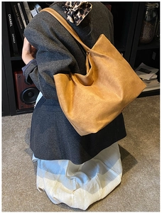 Close-up of a large tan suede tote bag worn by a model in a retro library setting