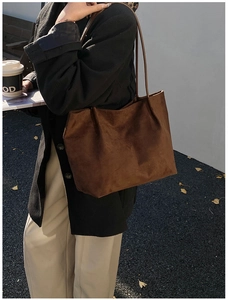 Close-up of a large dark brown suede tote bag worn over the shoulder in an autumn setting