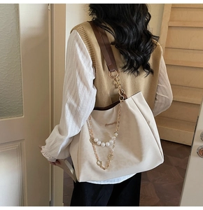 Detail of elegant beige tote bag featuring pearl chain, flower charm, and brown strap